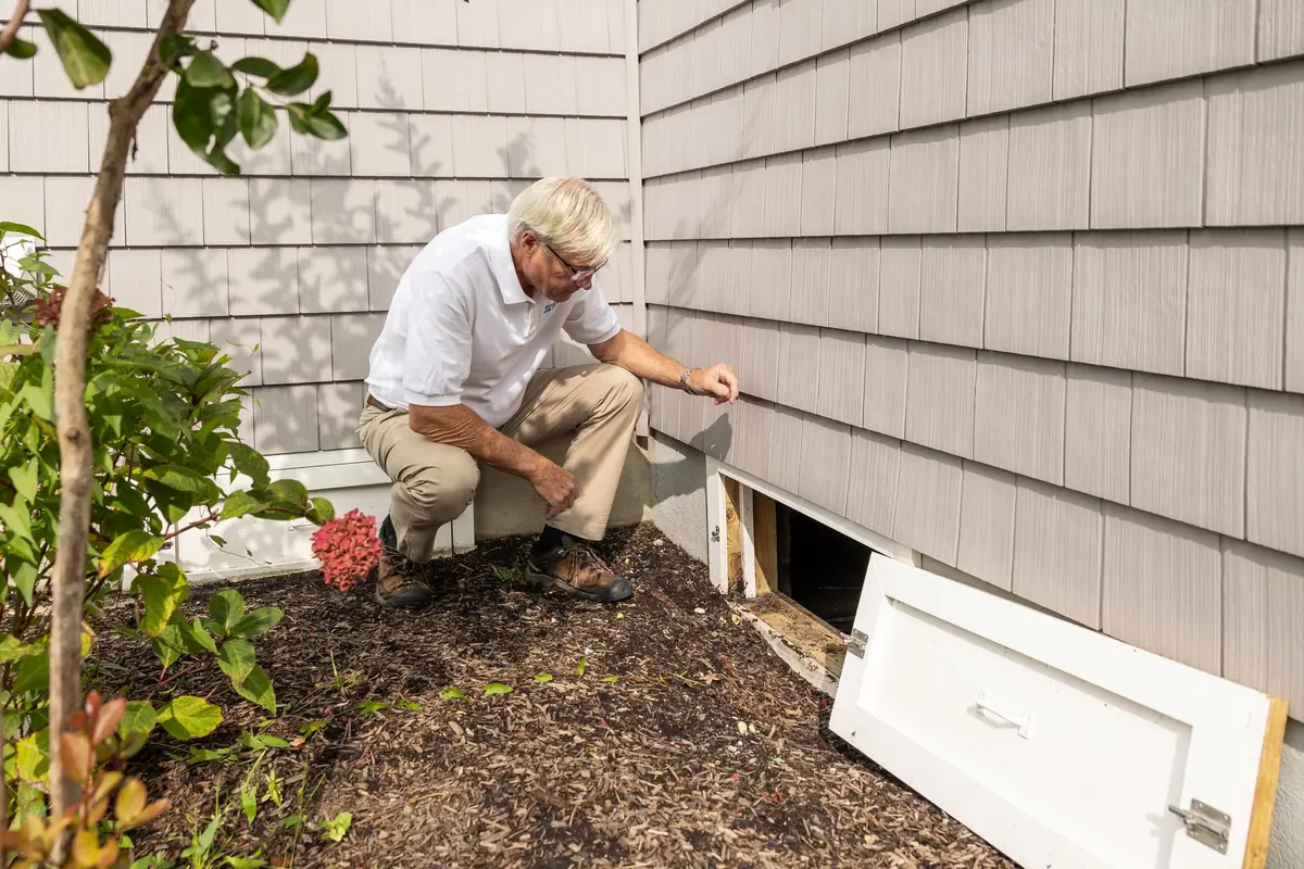 Inspector checking an open crawl space access along a home foundation