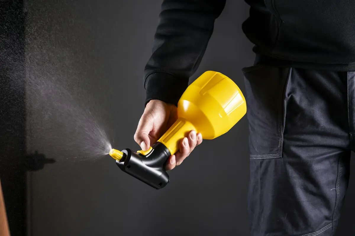 Technician in work clothes applying treatment with a handheld sprayer